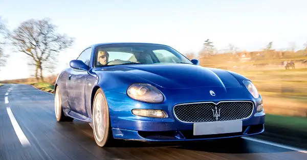 Blue Maserati GranSport cruising along a country road on a bright sunny day.